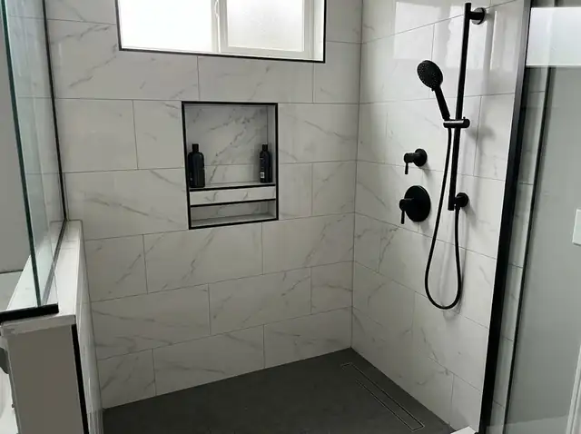 Re-tiled shower with white marble-look walls, black-trimmed niche and dark floor (illustration)