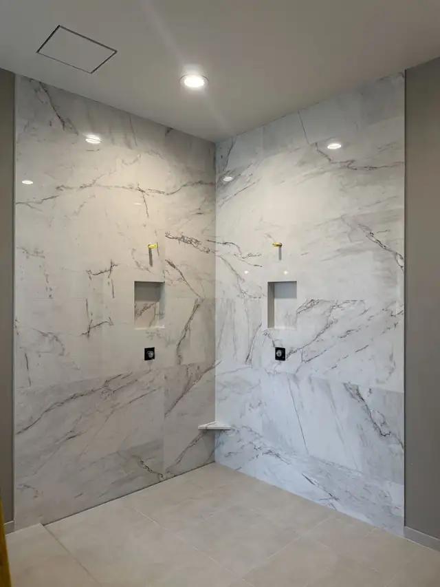 Shower walls in large marble-look porcelain with two recessed niches and matte black valves